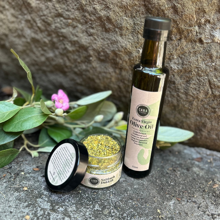Bottle of olive oil and a jar with a black lid on a stone surface with greenery in the background
