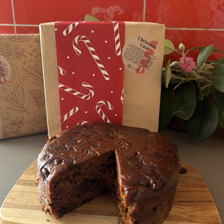 Chocolate cake with a slice removed on a wooden board, with a red and white candy cane patterned towel in the background.