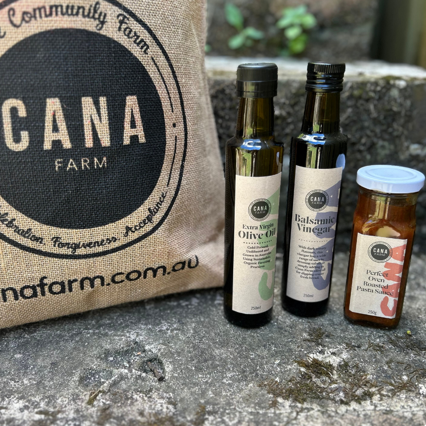 Three bottles of olive oil and vinegar from CANA Farm on a stone surface with a burlap bag in the background.