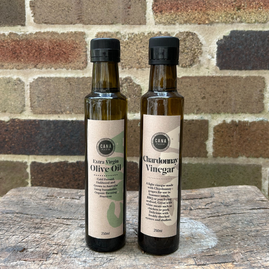 Two bottles of olive oil and vinegar on a wooden surface with a brick wall background.