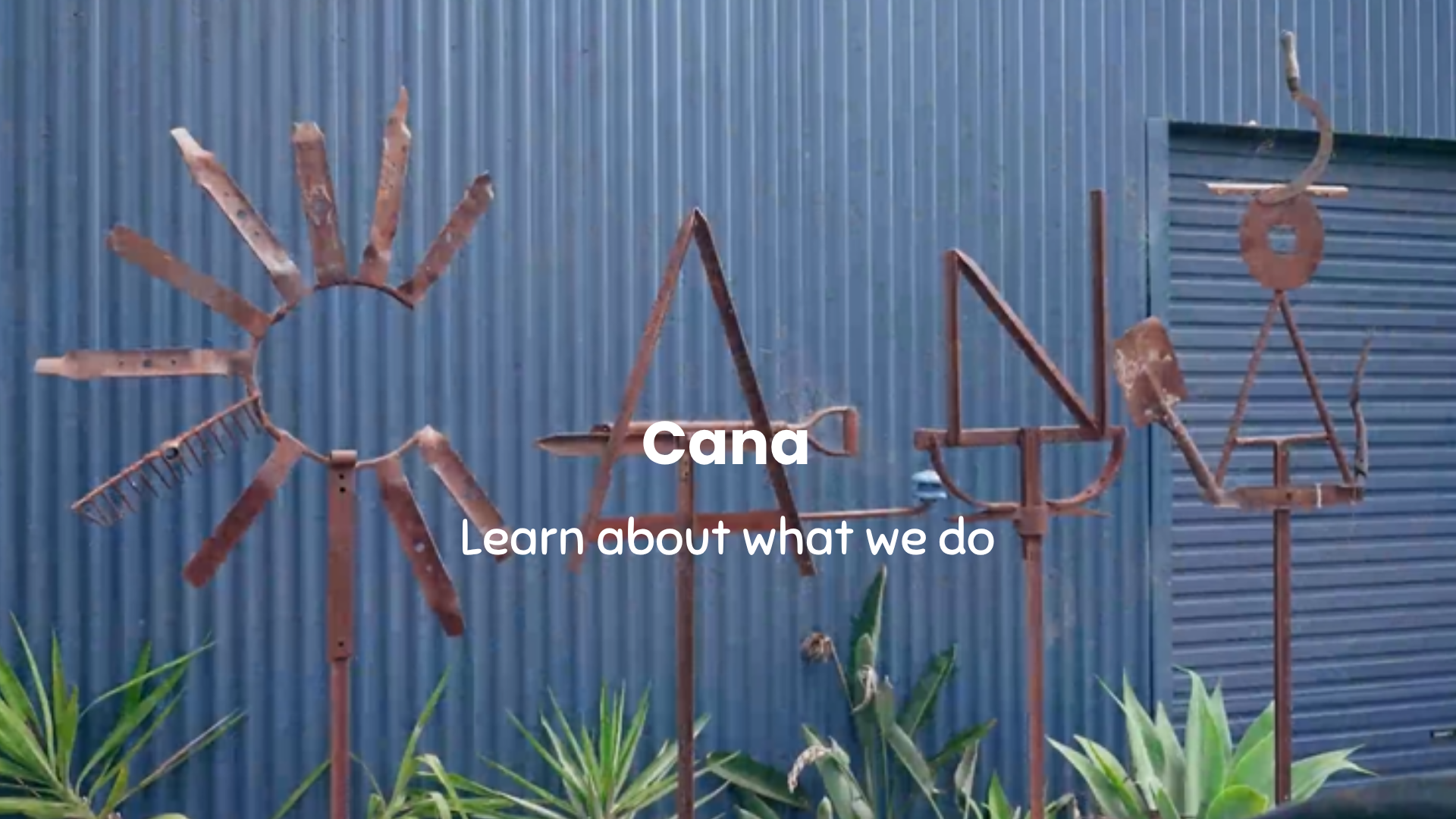 Decorative metal sculptures against a blue corrugated metal wall with 'Cana' branding.